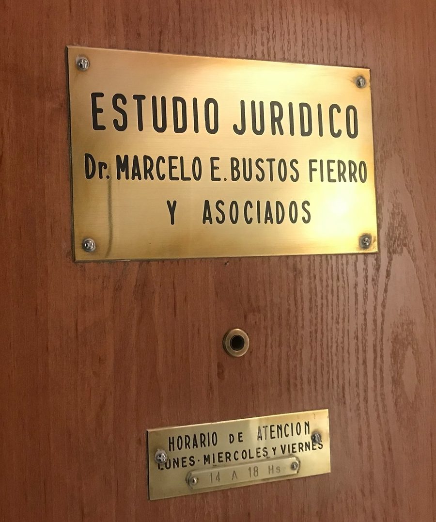 Placa de bronce del Estudio Jurídico Dr. Marcelo E. Bustos Fierro y Asociados en la puerta de la oficina, con el horario de atención debajo.
